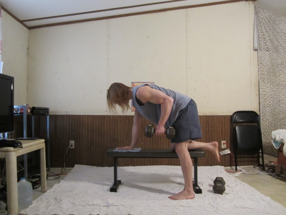 Dumbbell tricep kickback picture demonstrating the beginning of the repetition for the left arm from a side viewpoint.